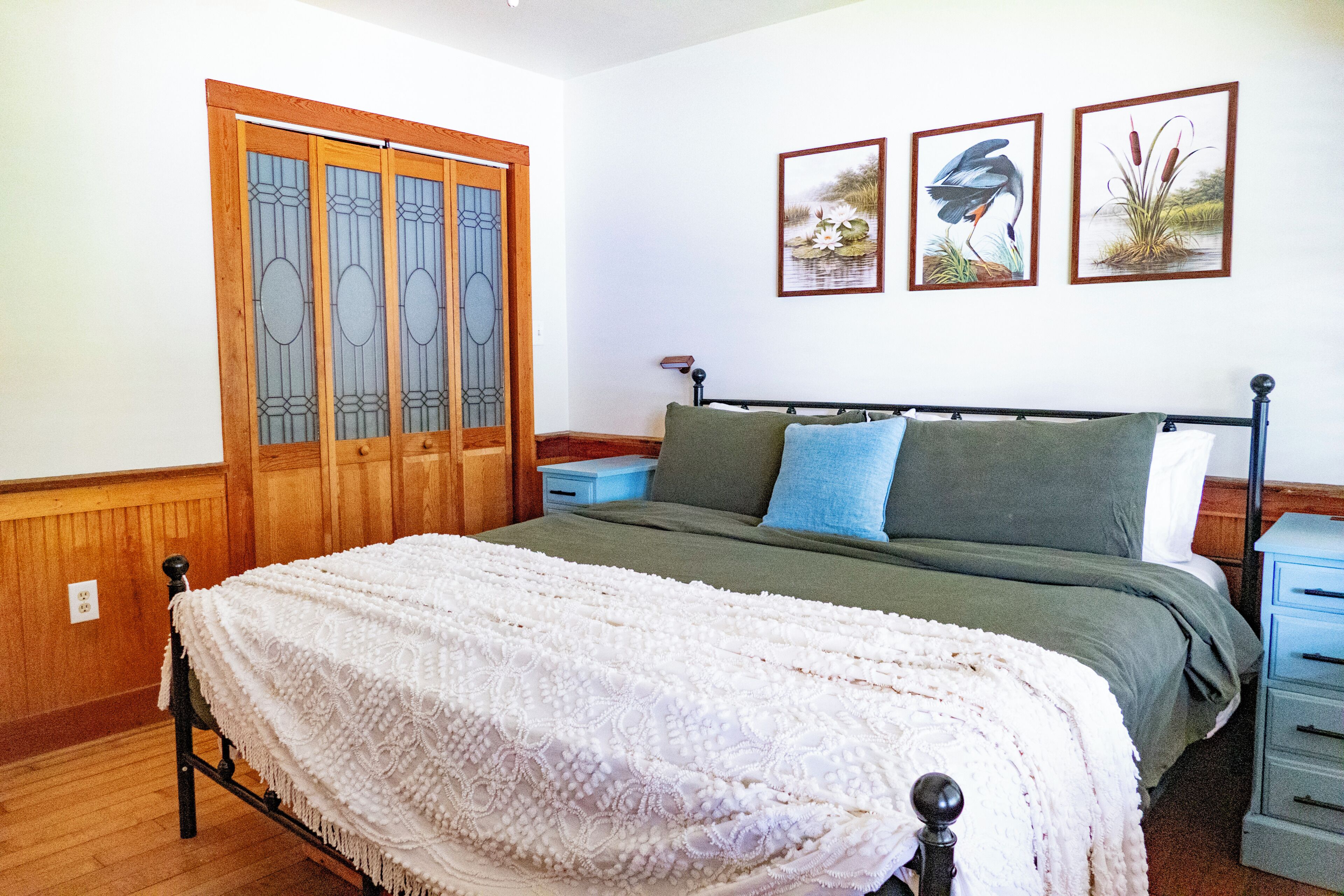 A bedroom with a bed, a nightstand, a dresser, and a window with a wooden door.