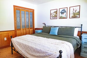 Ein Schlafzimmer mit Bett, Nachttisch, Kommode und Fenster mit Holztür.