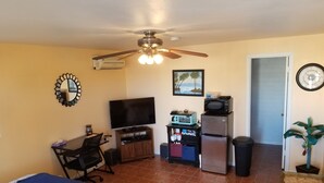 A compact living space with a bed, a desk, a television, a refrigerator, and a ceiling fan. - Quite studio with RV parking (Lake Havasu City)