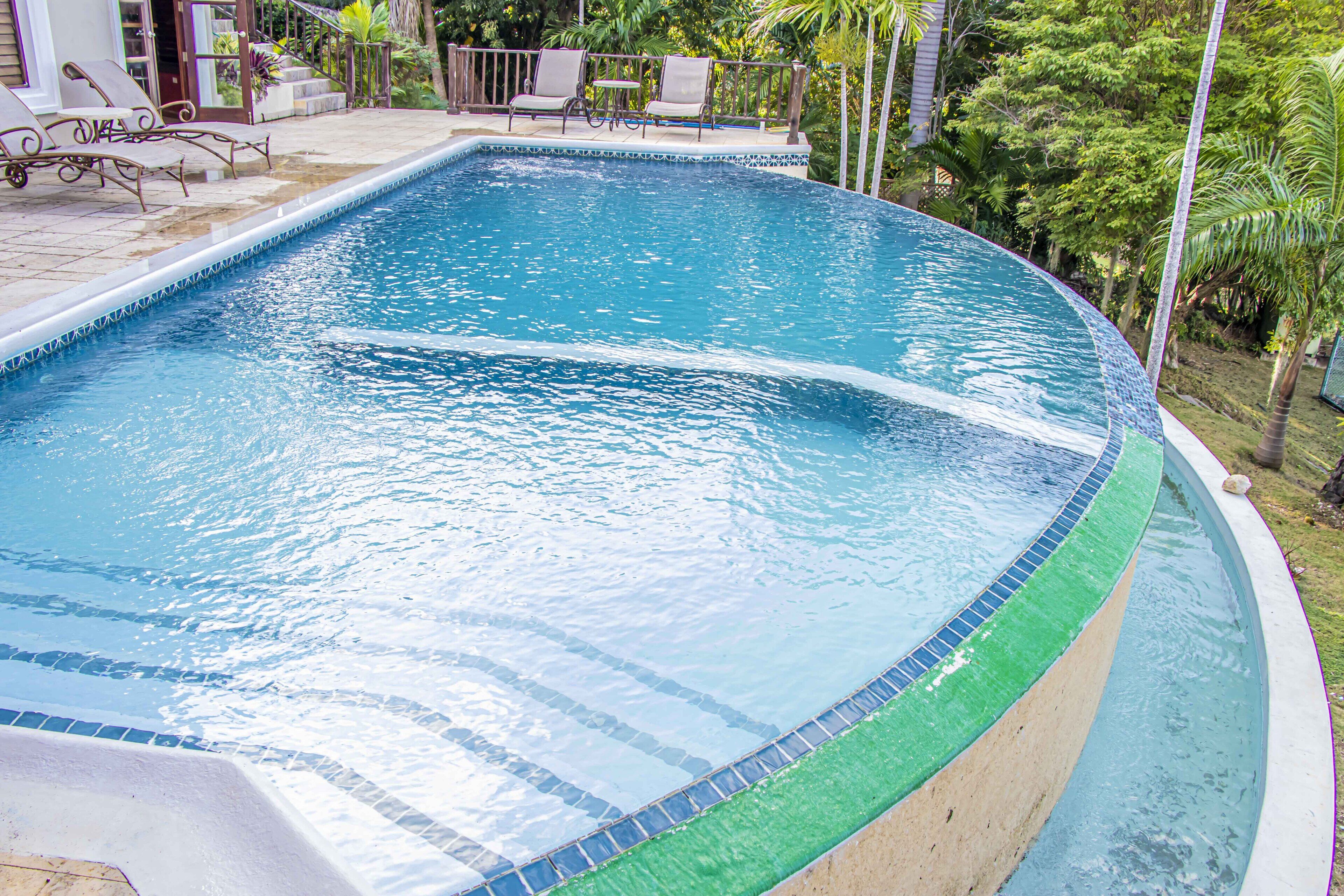 A swimming pool with a curved edge, surrounded by lounge chairs and a small table.