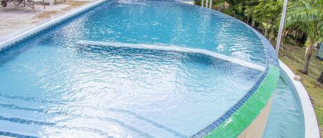 A swimming pool with a curved edge, surrounded by lounge chairs and a small table.
