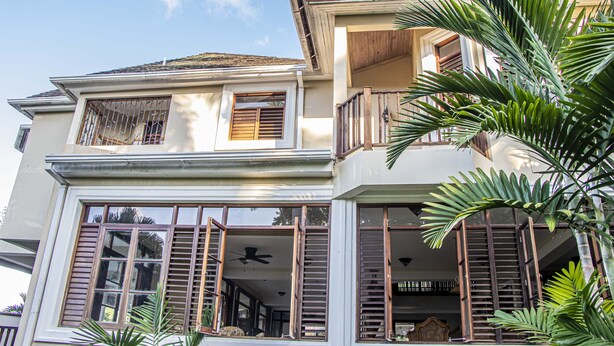 A two-story house with a balcony, large windows, and a ceiling fan.