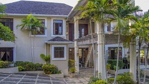 A two-story house with a balcony, a stone-paved driveway, and tropical landscaping. - Villa Belle Abri (Montego Bay)