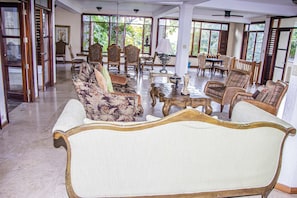 Relax in a spacious living area with a high ceiling and large windows, featuring a patterned sofa, chairs, and dining table for social gatherings.
