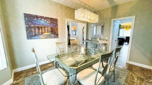 Une salle à manger avec une table en verre, des chaises, un lustre et un tableau au mur.