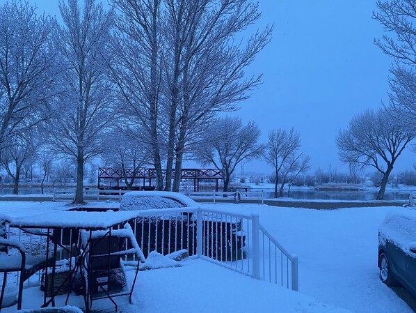 A snow-covered outdoor area with a wooden bench, a metal fence, and a car partially covered in snow.