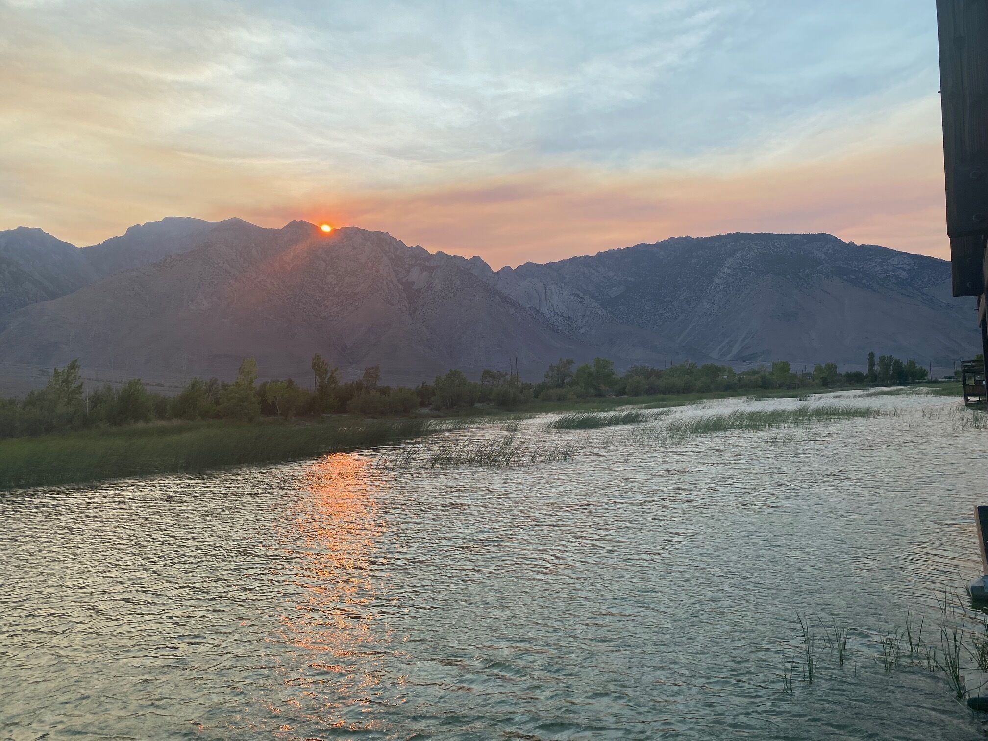 A river reflecting the sun with mountains in the background.
