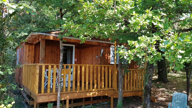 Une cabane en bois dotée d’une terrasse, entourée d’arbres.