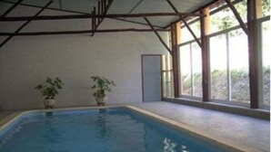 Une piscine intérieure à l’eau d’un bleu limpide, entourée de fenêtres et de plantes en pot.