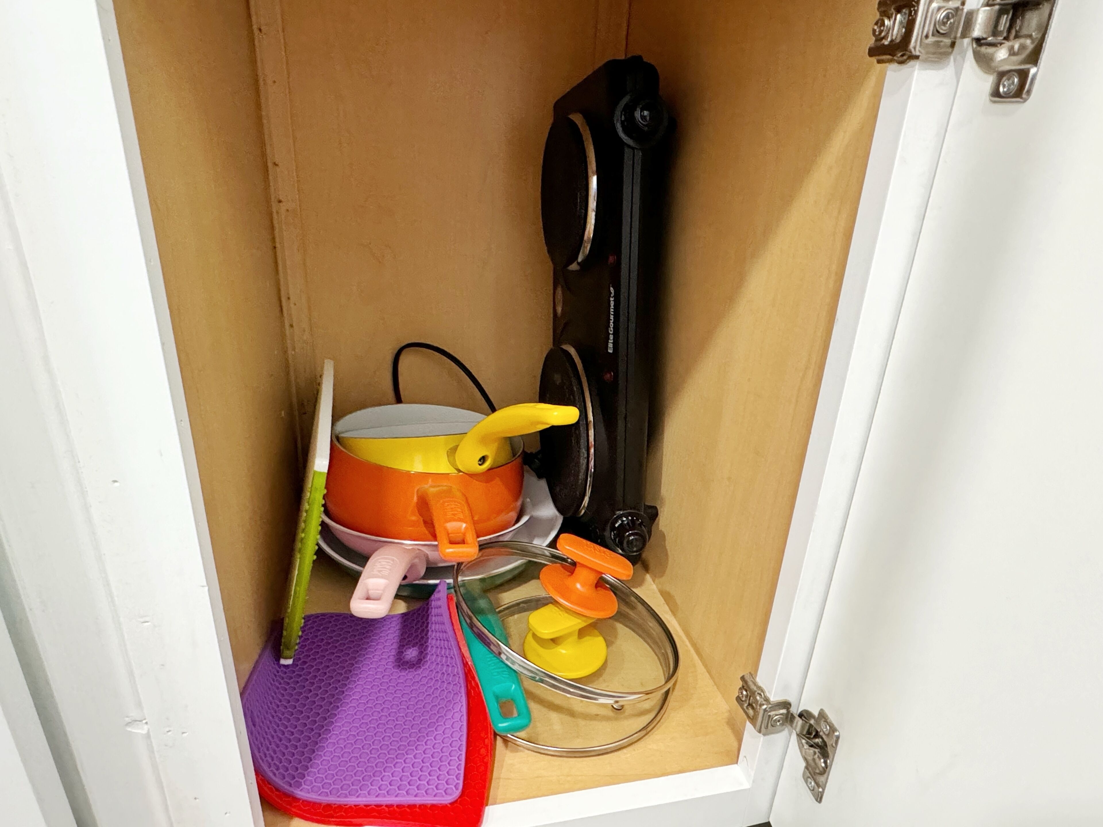 A kitchen cabinet with a pot, a spatula, a whisk, and a measuring cup.