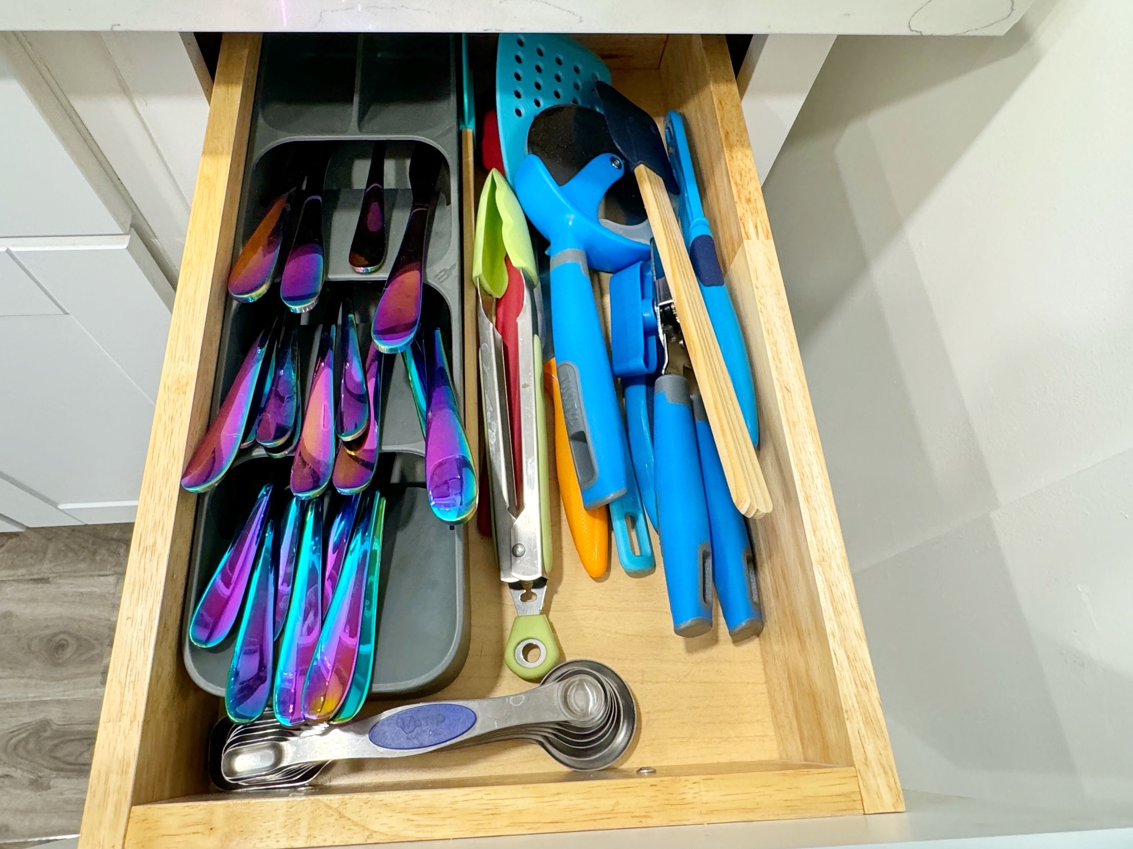 A drawer with kitchen utensils including spoons, spatulas, and a measuring cup.