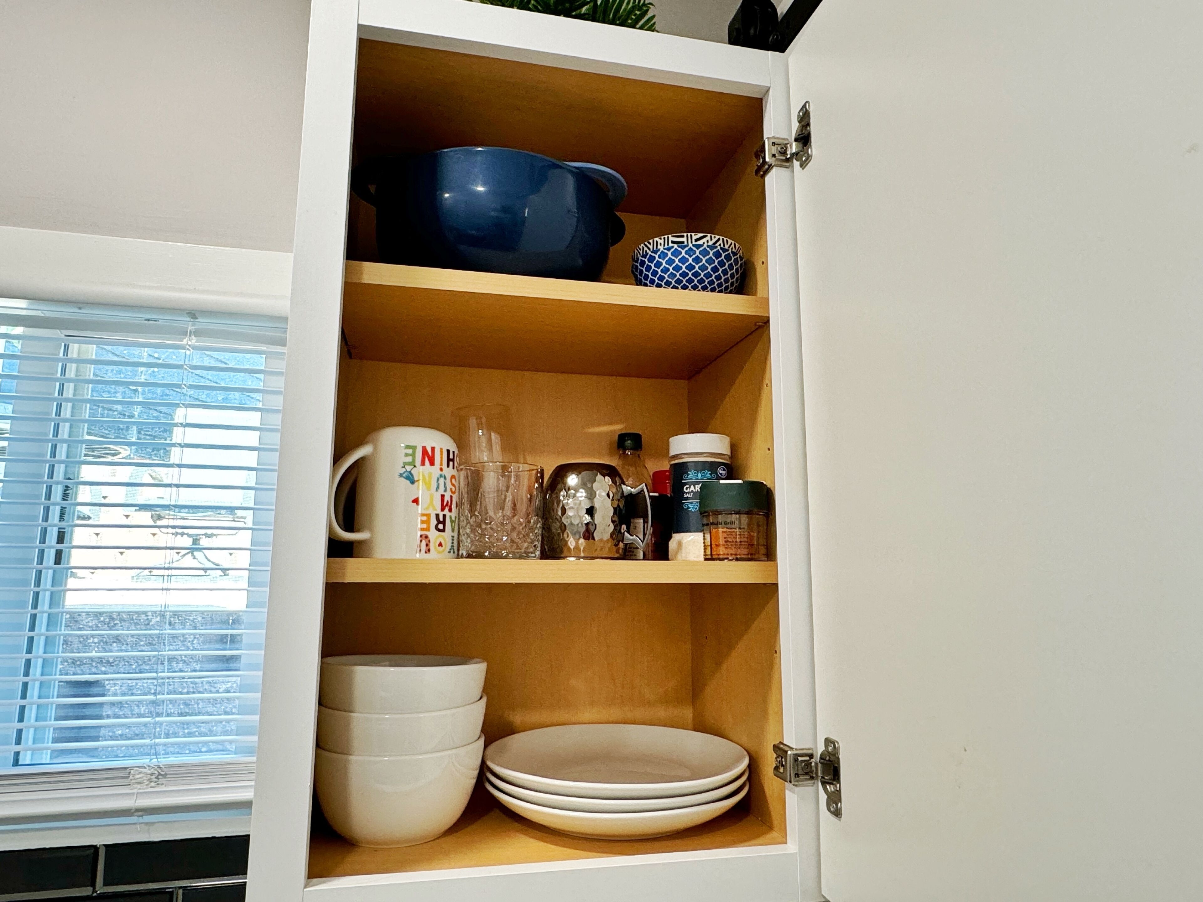 Un meuble de cuisine doté d’étagères contenant divers ustensiles de cuisine, notamment des bols, des assiettes, une tasse et un verre.