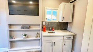 Una cucina moderna con mobili bianchi, una TV integrata, una finestra e un lavandino.