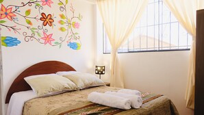 A neatly made bed with a floral wall decoration, a window with curtains, and a bedside lamp. - COZY & BEAUTIFUL APART IN SAN BLAS CUSCO (Cusco)