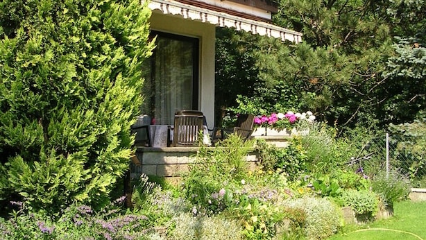 A house with a covered porch, surrounded by lush greenery and flowering plants. - Spacious,comfortable apartment,150m2, first floor,quiet,garden-side with terrace (Wien)