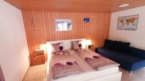 Ein Schlafzimmer mit Holzboden, einem Bett mit Blumenmuster-Bettwäsche, einem blauen Sofa, einem Nachttisch und einem an der Wand montierten Fernseher.