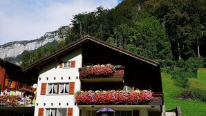 Eine zweistöckige Chalet mit Balkonen, die mit Blumen geschmückt sind, vor einer Bergkulisse.