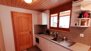 Eine Küche mit Holzschränken, einer Granitabdeckung, einer Spüle, einem Fenster mit Jalousien und einem Regal mit Küchenutensilien.