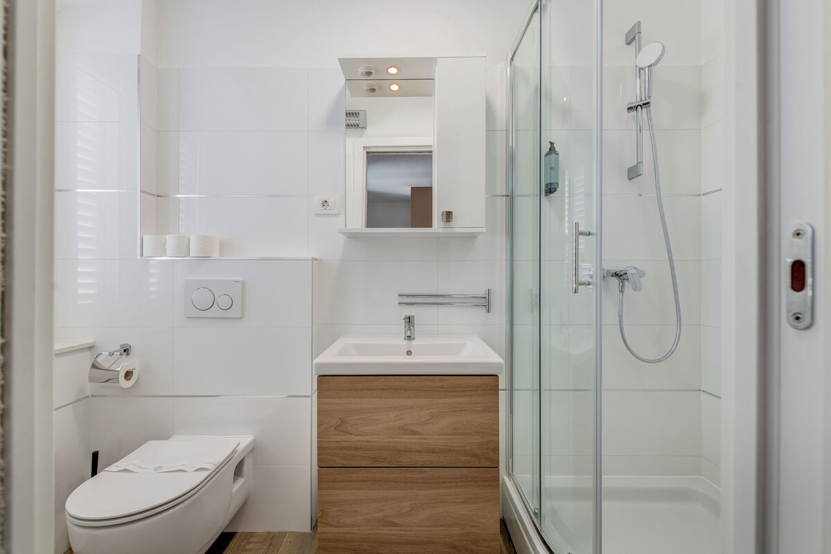 A modern bathroom with a toilet, sink, mirror, and glass-enclosed shower.