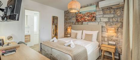 Een hotelkamer met een bed, nachtkastje, televisie en een stenen muur met een schilderij.