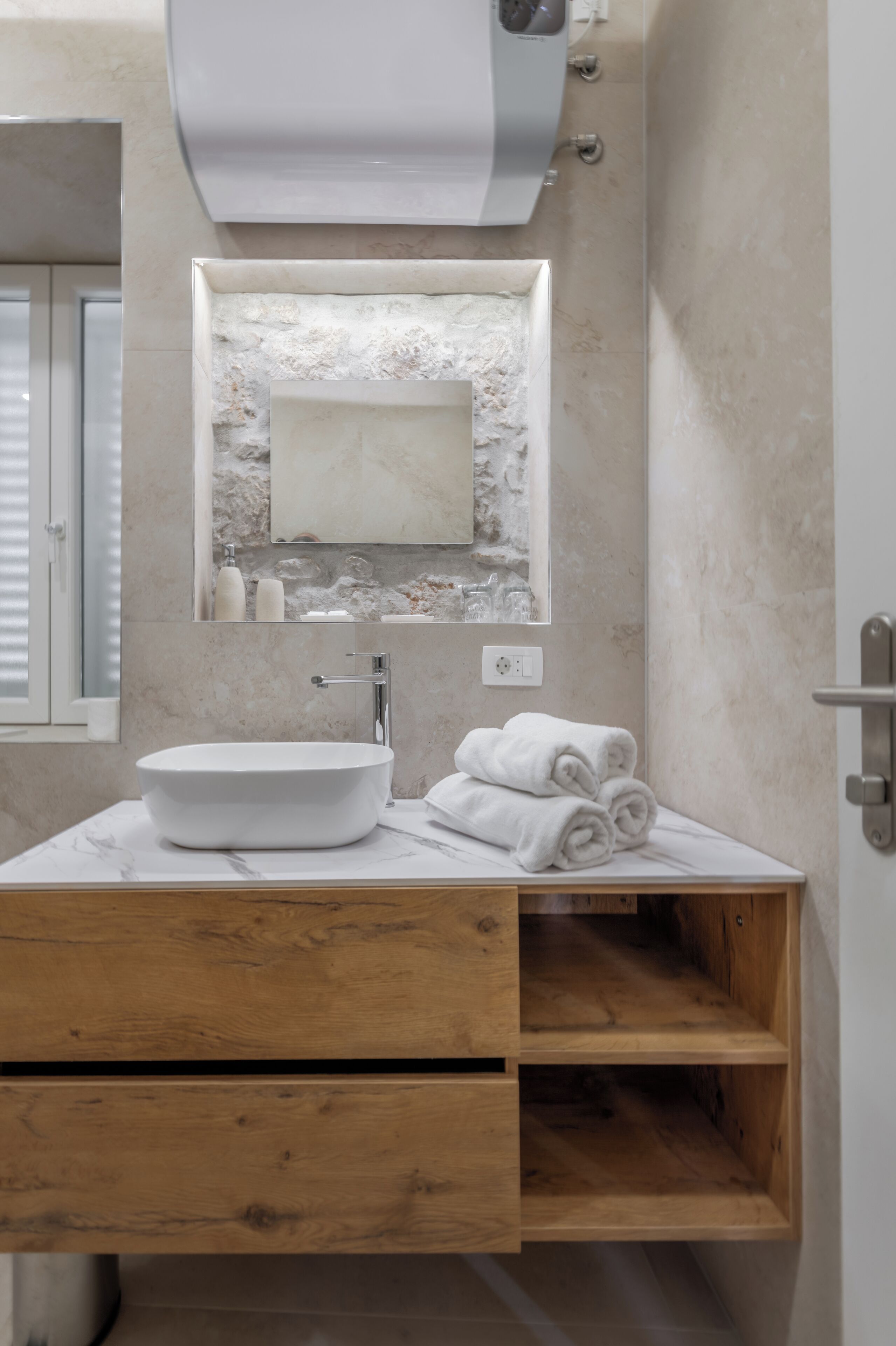 A bathroom with a white sink, marble countertop, wooden vanity, and a mirror with a stone backsplash.