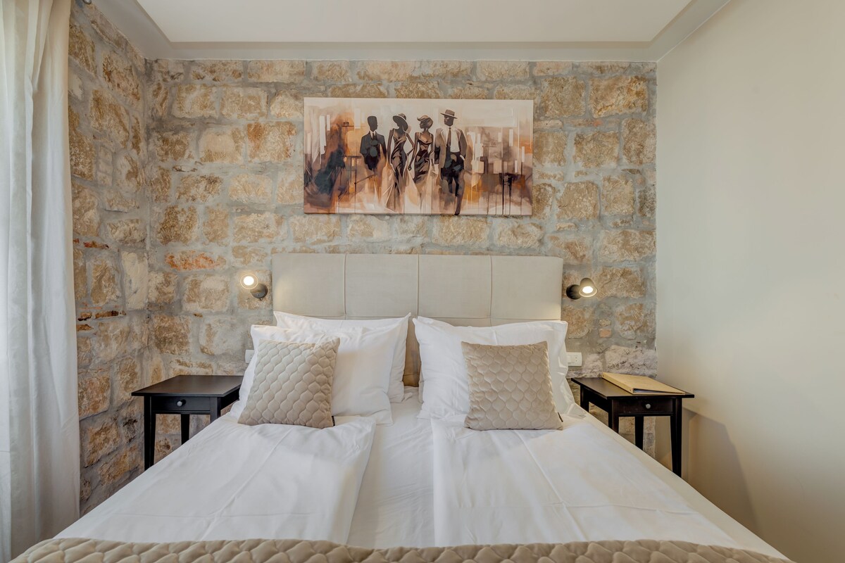 A double bed with two nightstands, a stone wall, and a painting above the bed.