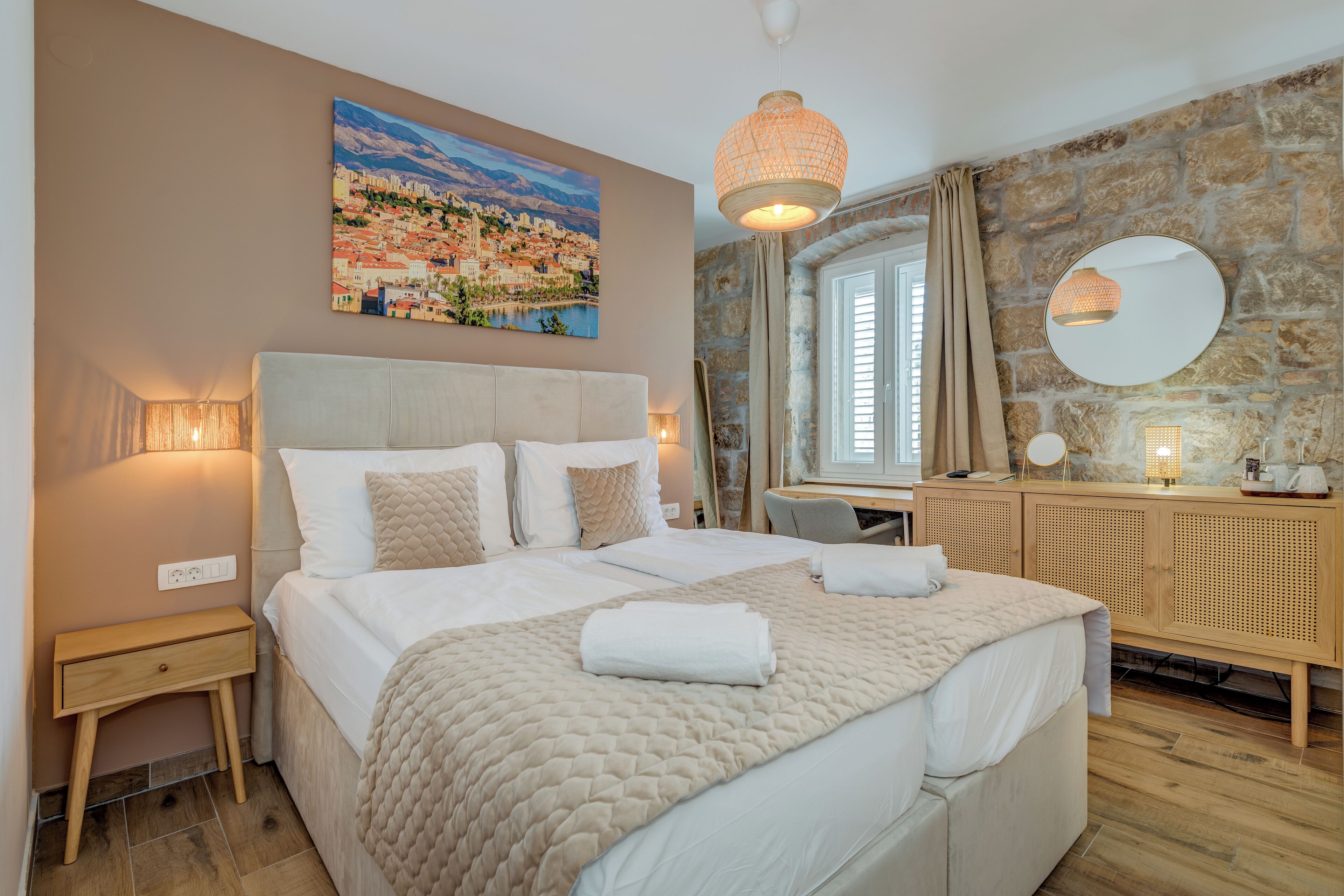 Une chambre bien aménagée, avec un grand lit, des tables de chevet, un bureau et un mur en pierre.