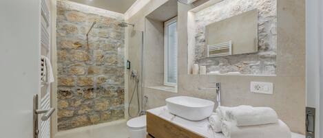 A modern bathroom with a stone shower wall, a white sink, and a wooden vanity.