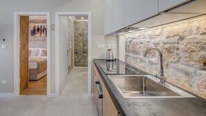 A modern kitchen with a stone accent wall, a stainless steel sink, and a wooden cabinet. - InMotion Luxury Rooms (Split)