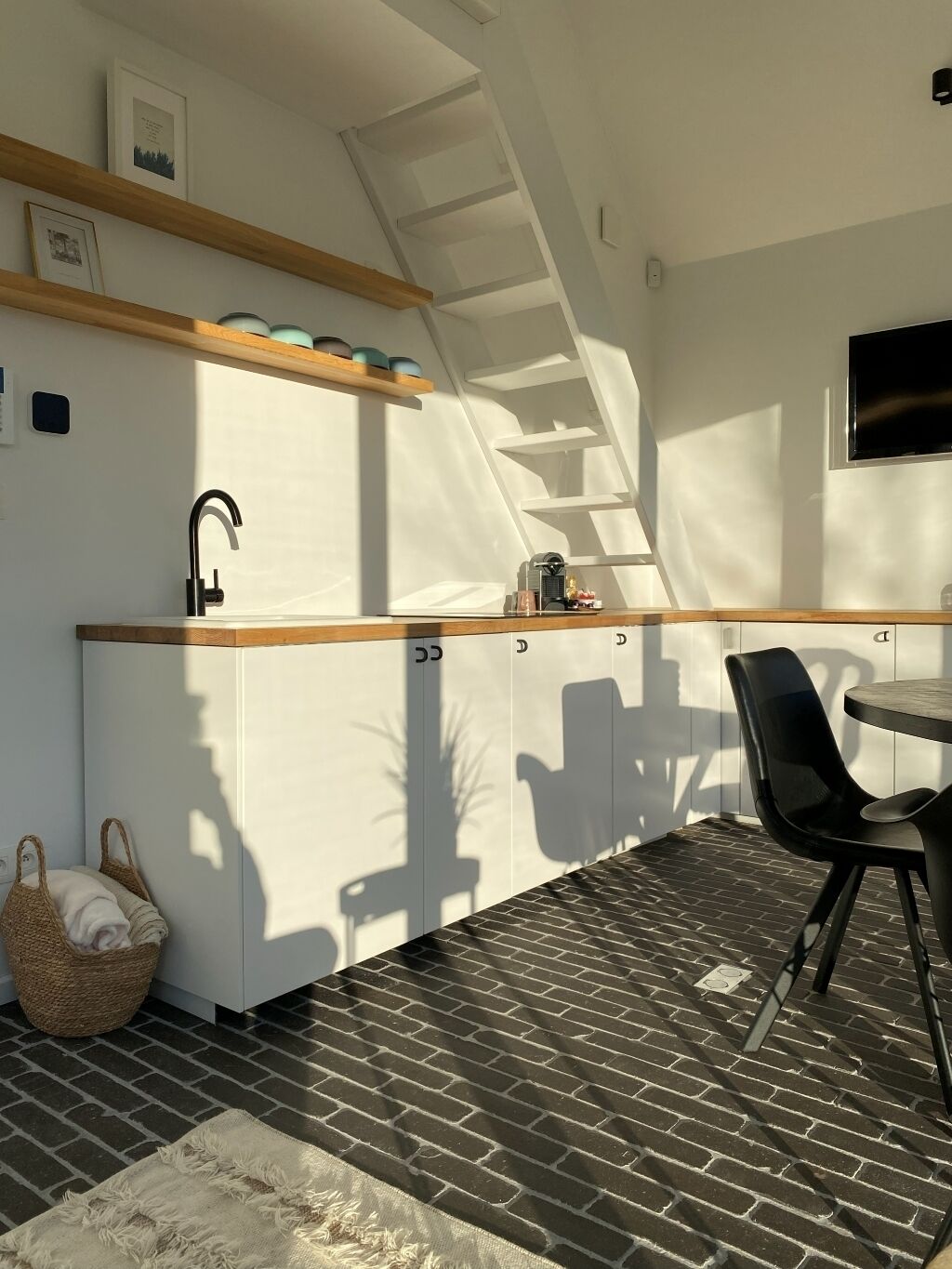 A compact kitchen with a built-in sink, wooden shelves, and a dining area with a table and chairs.