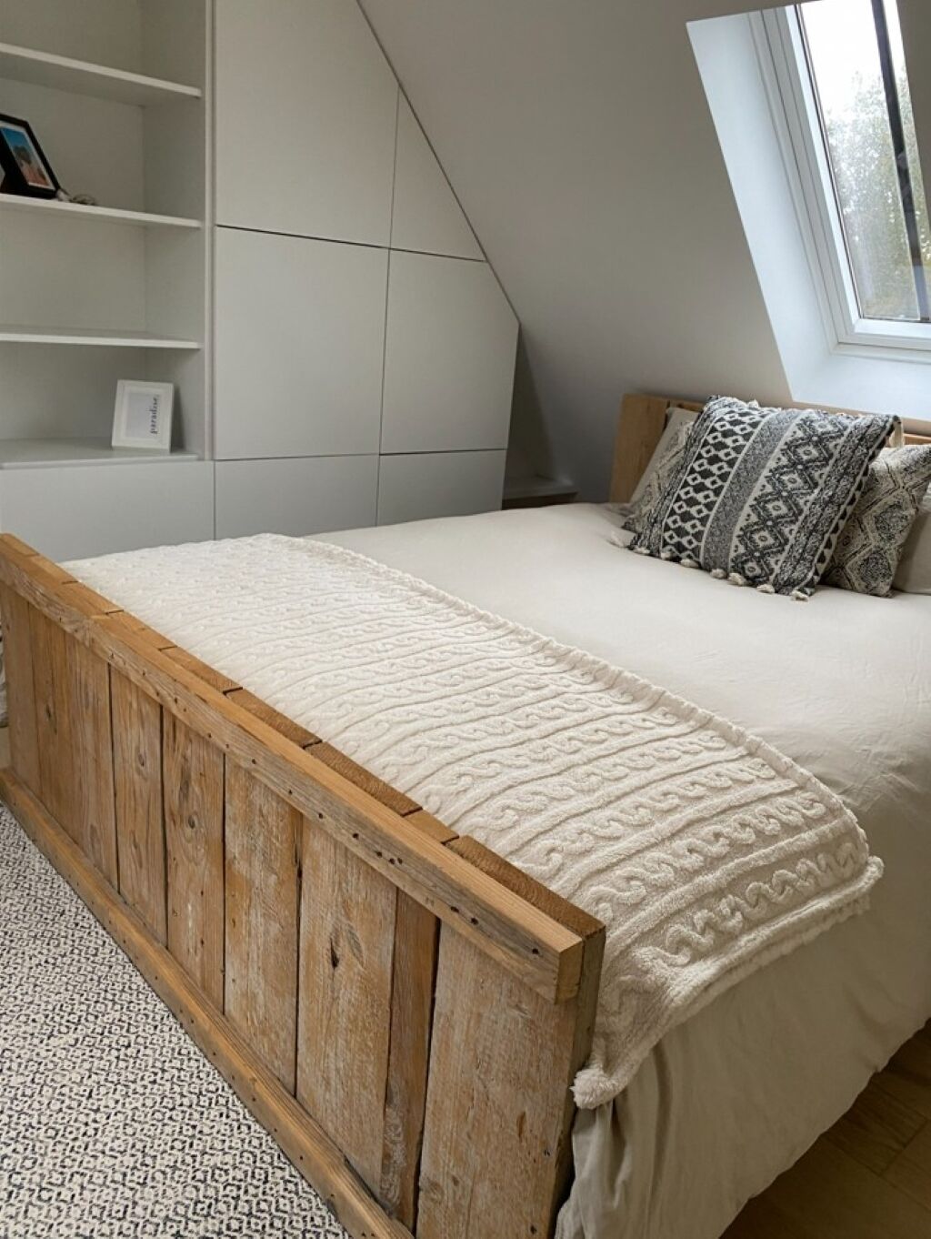 Una camera da letto con un letto con struttura in legno, una coperta bianca e cuscini decorati.