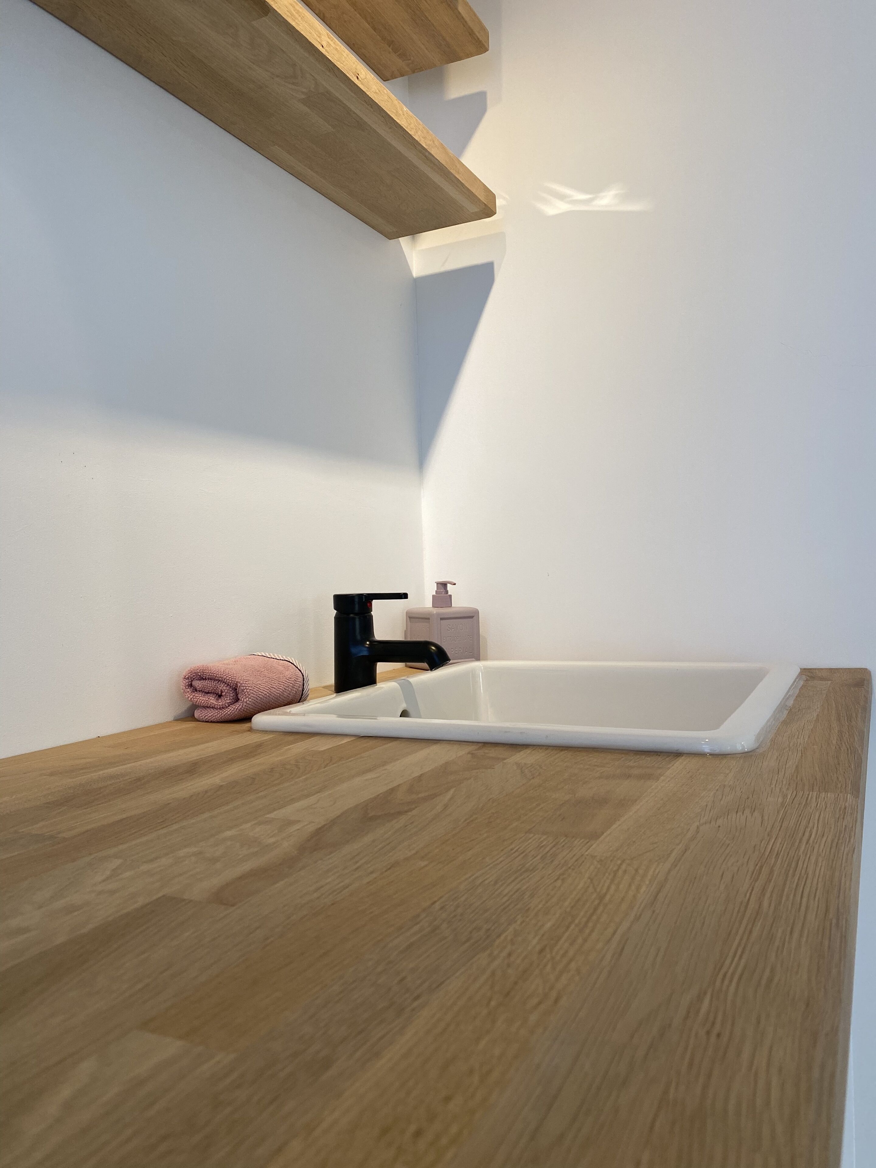 Une salle de bain avec un comptoir en bois, une baignoire blanche, un robinet noir et une serviette rose.