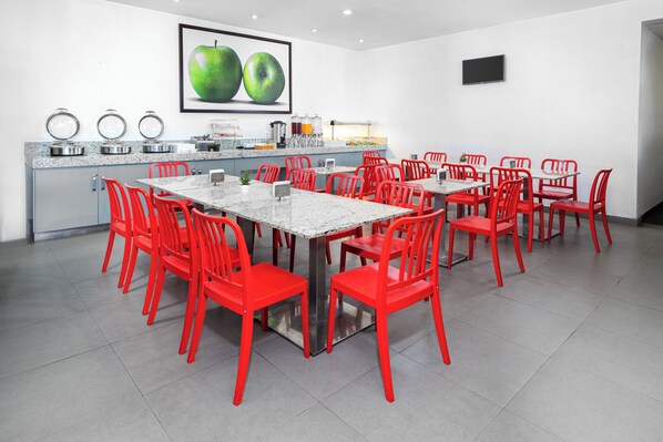 A modern dining area with red chairs and a marble table, a kitchen counter with appliances, and a large fruit-themed picture on the wall.