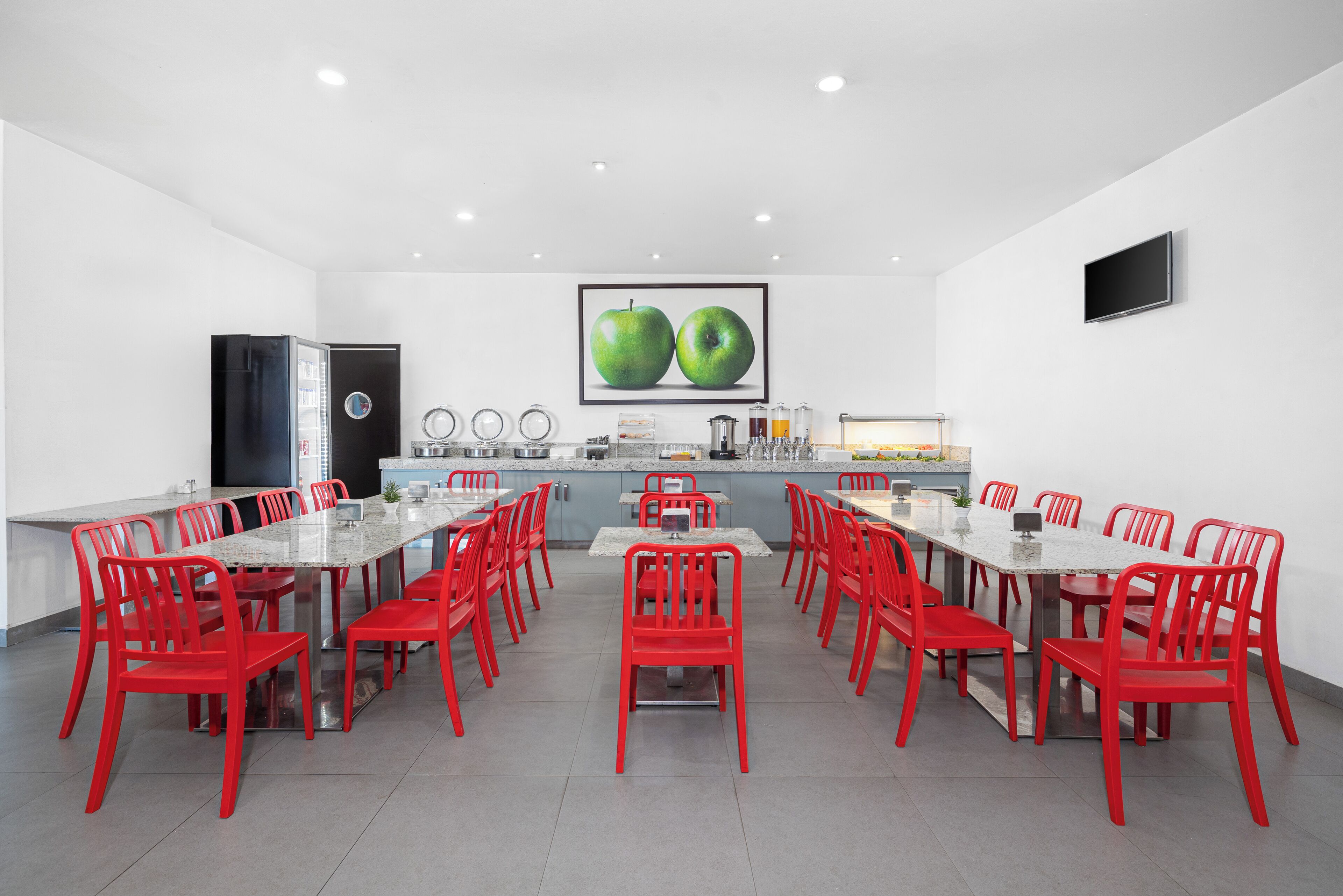 Une cuisine moderne avec une longue table à manger et des chaises rouges, un réfrigérateur et une grande fenêtre.
