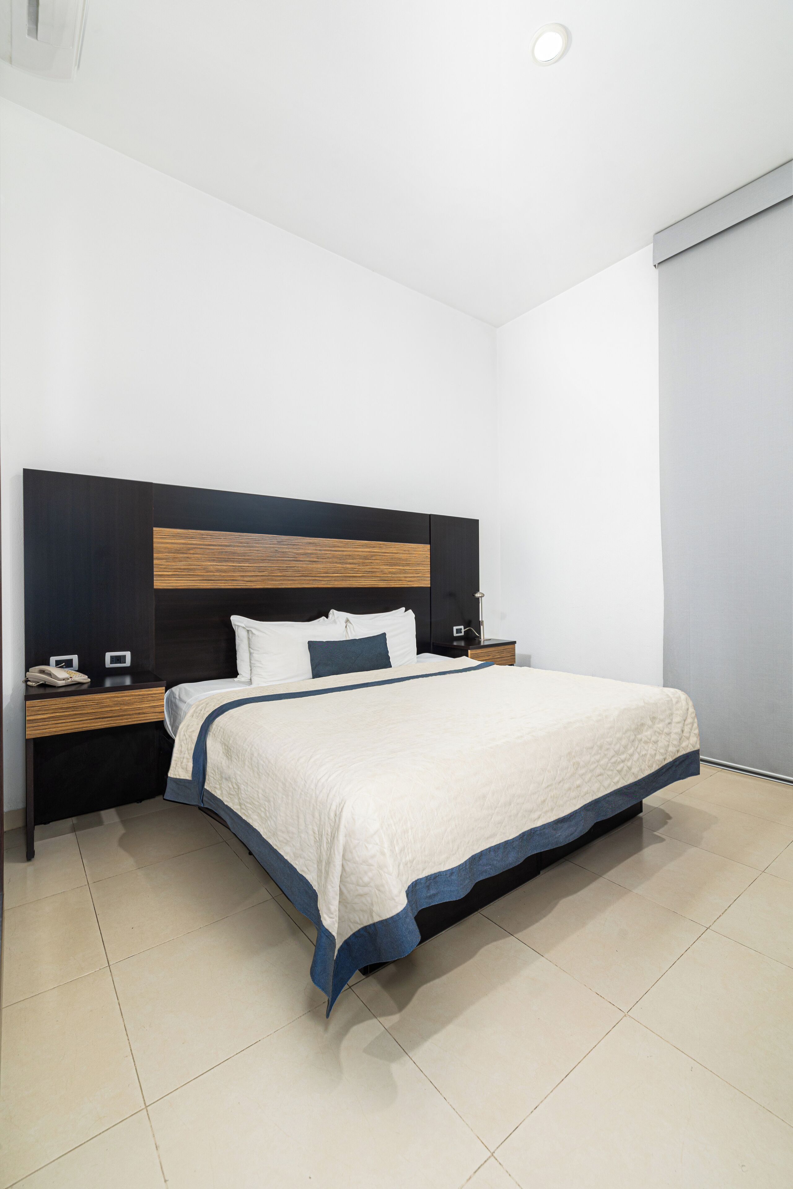 Habitación de hotel moderna con una cama grande, cabecera de madera, mesita de noche con teléfono y ventana con vistas.
