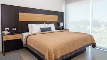 Una habitación de hotel moderna con una cama grande, una mesita de noche con un teléfono, un revistero y un banco.