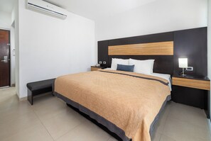 A hotel room with a bed, bedside tables, a bench, an air conditioning unit, and a nightstand with a lamp. - Hotel México Plaza Silao Aeropuerto (Silao)