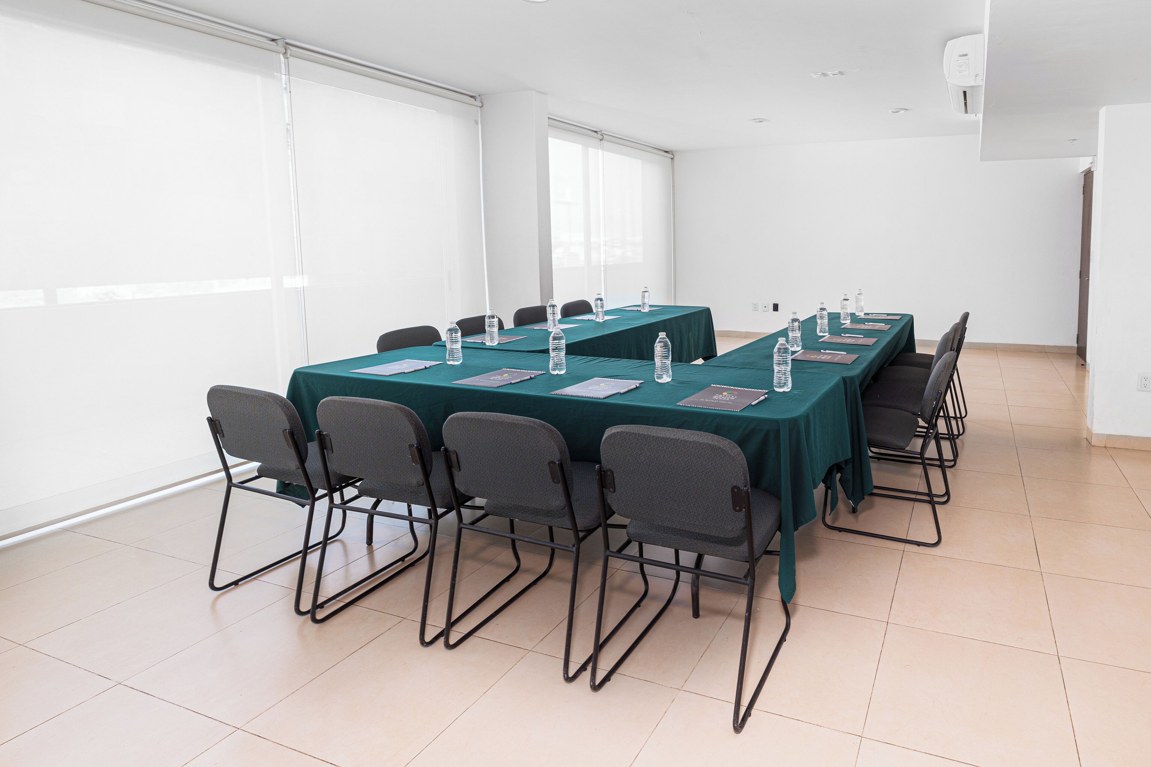 Un salón de conferencias con una larga mesa, sillas, botellas de agua y documentos.