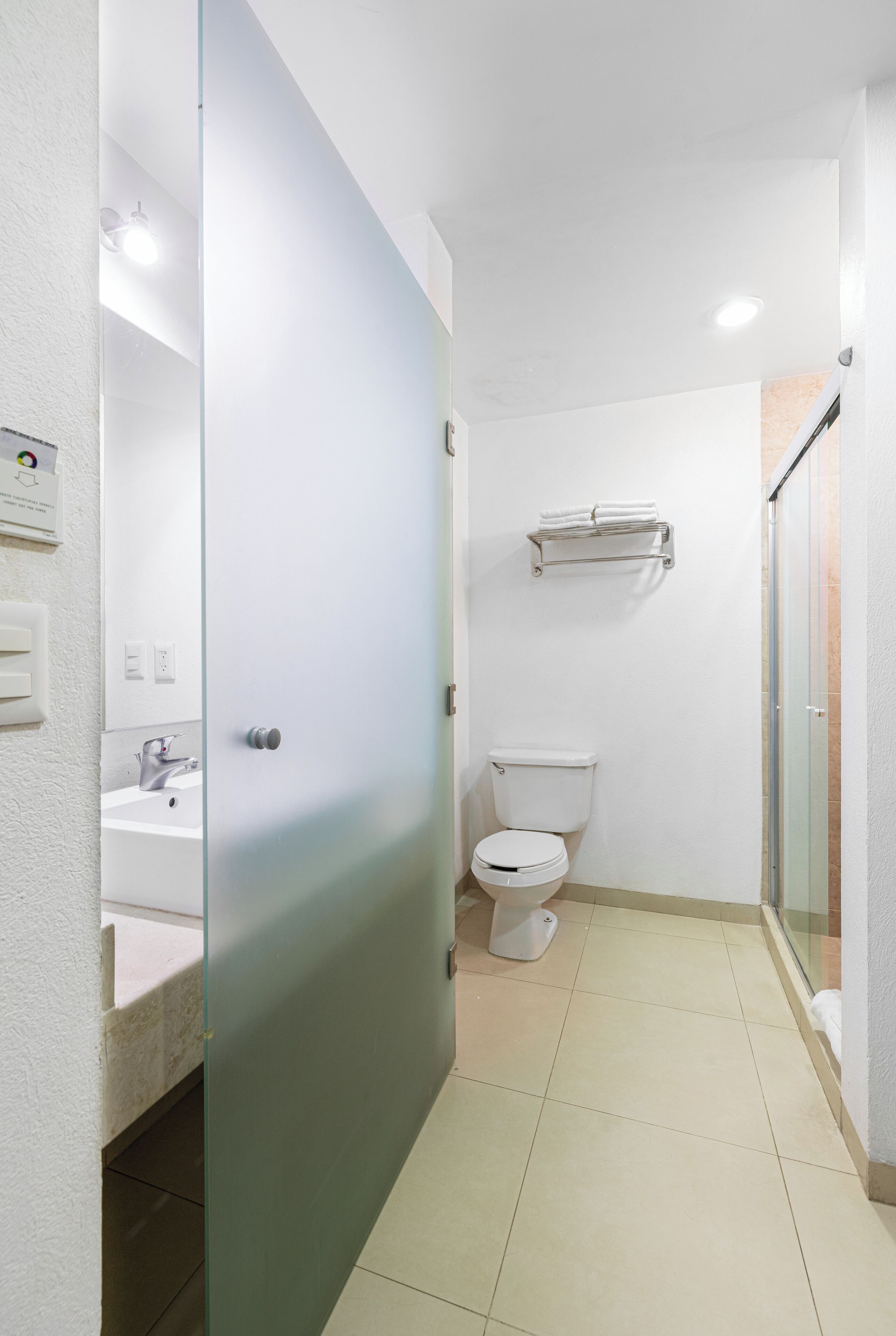 Une salle de bain moderne avec une porte en verre, un lavabo blanc, des toilettes et une douche à parois de verre.