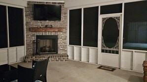 A stone fireplace with a television above it, a large window with a decorative frame, and a door with a screen. - Charming Beach-Themed Studio Apartment in Doerun, GA with Private Pool (Doerun)