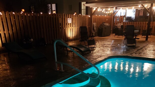 A swimming pool with a blue light, a wooden fence, and outdoor seating. - Charming Beach-Themed Studio Apartment in Doerun, GA with Private Pool (Doerun)
