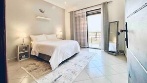 A bedroom with a bed, bedside tables, a mirror, and a view of the outside. - Shilo Space-Emerald Apt.Free WiFi & Modern Look. (Kampala)