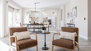 A spacious living room with two brown leather armchairs, a round coffee table, and a dining area in the background. - Fun Filled Stadium Getaway w/ Heated Pool & Golf (Glendale)