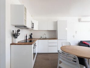 A modern kitchen with white cabinets, a wooden countertop, and a dining area with a table and chairs. - Elaia Phoebé in the Mediterranean – 14-meter heated pool (TOUROUZELLE 11200)