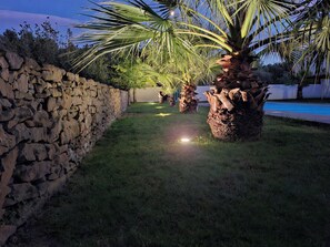 A stone wall, a grassy lawn, and palm trees. - Elaia Phoebé in the Mediterranean – 14-meter heated pool (TOUROUZELLE 11200)