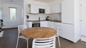Une cuisine moderne avec des meubles blancs, une table à manger en bois et un luminaire suspendu.