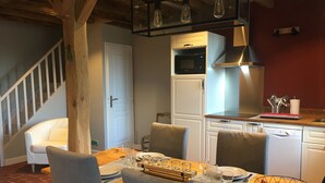 A dining area with a wooden table set for four, a kitchen with modern appliances, and a staircase leading to another level. - 18th century character gîte in the VAL DE CHAMBORD at the gates of Chambord (Huisseau-sur-Cosson)