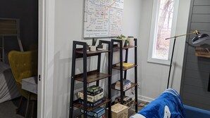 A room with a blue sofa, a bookshelf with board games, a map on the wall, and a window with a view of trees. - Newly Rennovated Home next to Zoo and Downtown Stadiums (Indianapolis)