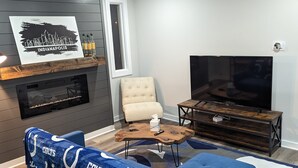 A modern living room with a blue sofa, a wooden coffee table, a TV, and a fireplace. - Newly Rennovated Home next to Zoo and Downtown Stadiums (Indianapolis)