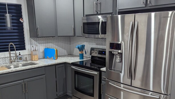 A modern kitchen with grey cabinets, stainless steel appliances, a microwave, oven, and a refrigerator. - Newly Rennovated Home next to Zoo and Downtown Stadiums (Indianapolis)